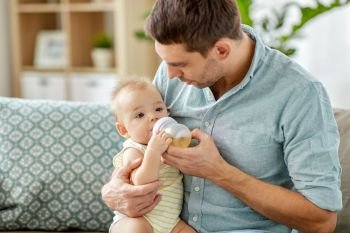family, fatherhood and people concept - father helping little baby daughter with drinking from bottle at home. father and baby drinking from bottle at home