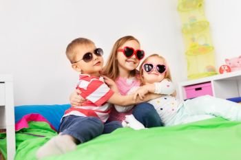 summer, valentines day and childhood concept - happy little kids in heart shaped sunglasses hugging at home. happy little kids in sunglasses hugging at home