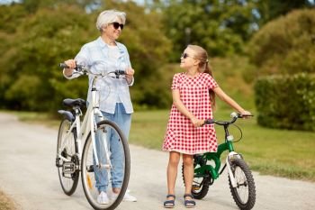 family, leisure and people concept - happy grandmother and granddaughter with bicycles at summer park. grandmother and granddaughter with bicycles