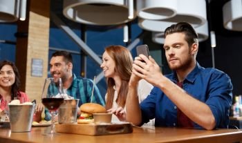 technology, lifestyle and people concept - man dining with friends and messaging on smartphone at restaurant. man messaging on smartphone at restaurant