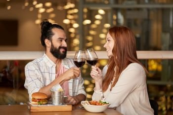 celebration, leisure and holidays concept - happy young couple eating and clinking glasses of red wine at restaurant. couple eating and drinking red wine at restaurant
