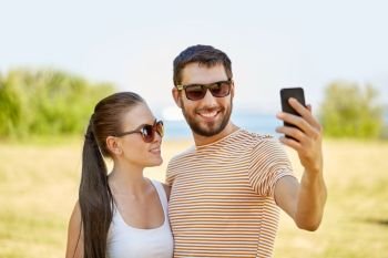 technology and people concept - happy couple taking selfie by smartphone in summer. happy couple taking selfie by smartphone in summer