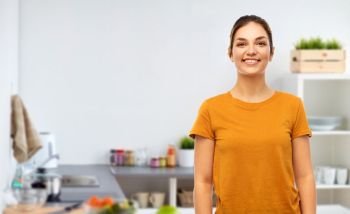 cooking and people concept - smiling young woman or teenage girl in blank orange t-shirt over home kitchen background. teenage girl in orange t-shirt over kitchen