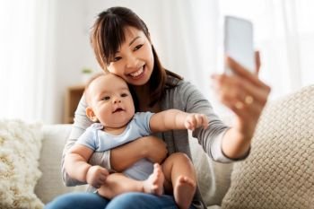 family, technology and motherhood concept - happy young asian mother with little baby son taking selfie by smartphone at home. happy mother with baby son taking selfie at home