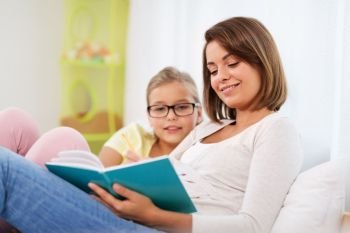 people, family and education concept - happy daughter with mother reading book at home. happy girl with mother reading book at home