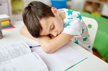 education, childhood and school concept - tired student boy sleeping on table at home. tired student boy sleeping on table at home