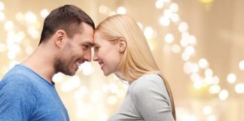 love and people concept - smiling couple standing forehead to forehead over beige background with festive lights. couple forehead to forehead over festive lights