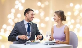 people and leisure concept - smiling couple eating appetizers at restaurant over festive lights on beige background. smiling couple eating appetizers at restaurant