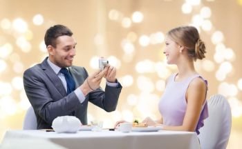 couple, technology and leisure concept - smiling man taking picture of wife or girlfriend by digital camera at restaurant over festive lights on beige background. man photographing woman by camera at restaurant