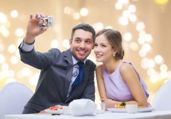 technology, valentines day and people concept - happy couple taking selfie by digital camera at sushi restaurant over festive lights on beige background. happy couple taking selfie at sushi restaurant