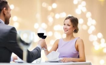 dating, celebration and valentines day concept - smiling young couple clinking glasses of non-alcoholic red wine and looking at each other at restaurant over festive lights on beige background. young couple with glasses of wine at restaurant