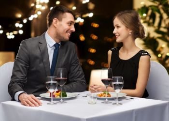 people and leisure concept - smiling couple with food and non-alcoholic red wine talking at restaurant over festive lights on background. couple with food and red wine at restaurant