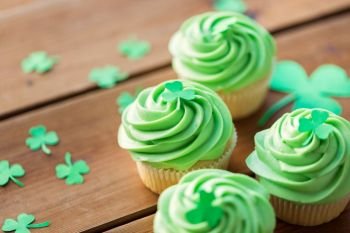 st patricks day, food and holidays concept - close up of green cupcakes and shamrock on wooden table. green cupcakes and shamrock on wooden table