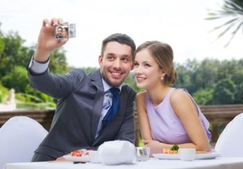 technology, valentines day and people concept - happy couple taking selfie by digital camera at sushi restaurant over summer background. happy couple taking selfie at sushi restaurant
