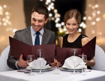 dating, luxury and people concept - happy couple with menus at restaurant over festive lights on background. couple with menus at restaurant