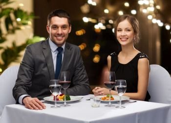 people and leisure concept - smiling couple with food and non-alcoholic red wine at restaurant over festive lights on background. couple with food and red wine at restaurant
