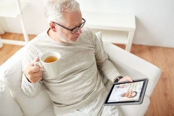 medicine, technology and healthcare concept - senior man having video chat with pharmacist on tablet pc computer and drinking tea at home. senior man having video chat with pharmacist