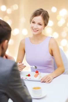 people and leisure concept - smiling woman looking at man and eating cake at restaurant over festive lights on beige background. woman looking at man and eating cake at restaurant