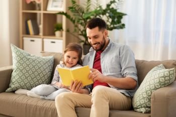 family, leisure and people concept - happy father and daughter reading book at home. happy father and daughter reading book at home