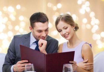 dating, luxury and people concept - happy couple with menu at restaurant over festive lights on beige background. couple with menu at restaurant