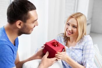 surprise, valentines day and people concept - happy couple with gift box at home. happy couple with gift box at home