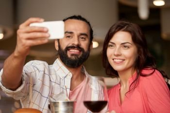 leisure, technology and people concept - happy couple having lunch and taking selfie by smartphone at restaurant. couple taking selfie by smartphone at restaurant