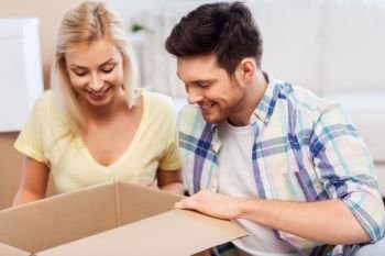 mortgage, moving and real estate concept - happy couple looking inside box or parcel at home. happy couple looking inside box or parcel at home