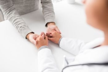 medicine, healthcare and old age concept - close up of young doctor holding senior patient hand. close up of doctor holding senior patient hand