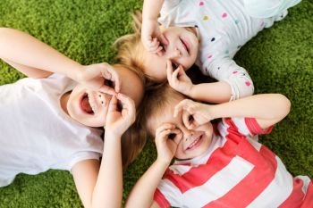childhood, leisure and family concept - happy little kids lying on floor or carpet and looking through finger glasses. happy little kids looking through finger glasses
