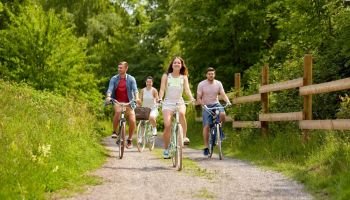 people, leisure and lifestyle concept - happy young friends riding fixed gear bicycles on country road in summer. happy friends riding fixed gear bicycles in summer