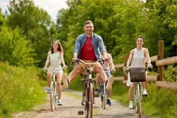 people, leisure and lifestyle concept - happy young friends riding fixed gear bicycles on country road in summer. happy friends riding fixed gear bicycles in summer