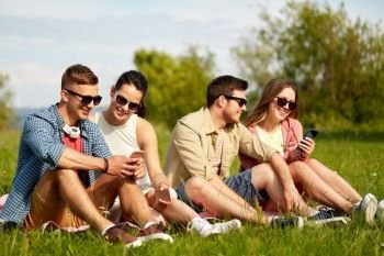 friendship, technology and leisure concept - group of smiling friends with smartphones sitting on grass in summer. smiling friends with smartphones sitting on grass