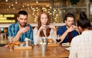 leisure, technology, lifestyle and people concept - friends with smartphones dining at restaurant. friends with smartphones at restaurant