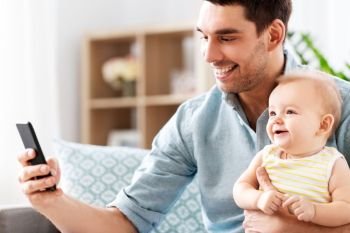 family, fatherhood and technology concept - father with little baby daughter using smartphone at home. father with baby daughter using smartphone at home