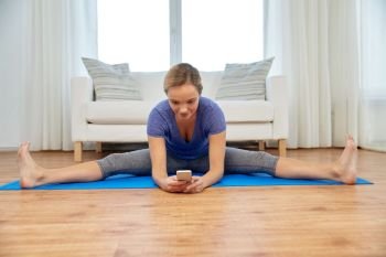 fitness, technology and gymnastics concept - woman with smartphone doing yoga or split exercise at home. woman with smartphone doing yoga at home