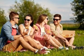 friendship, leisure and food concept - group of smiling friends eating pizza at picnic in summer park. friends eating pizza at picnic in summer park