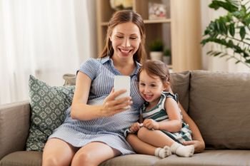 pregnancy, people and family concept - happy pregnant mother and little daughter with smartphone at home. pregnant mother and daughter with smartphone