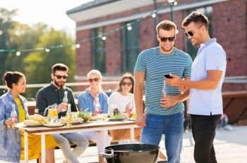 leisure and people concept - happy friends with smartphone having barbecue party on rooftop in summer. happy friends having bbq party on rooftop