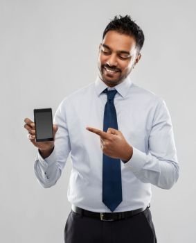 business, office worker and people concept - smiling indian businessman pointing finger to blank screen of smartphone over grey background. indian businessman with smartphone