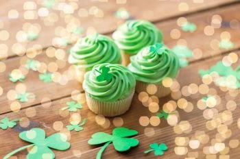 st patricks day, food and holidays concept - green cupcakes and shamrock on wooden table. green cupcakes and shamrock on wooden table