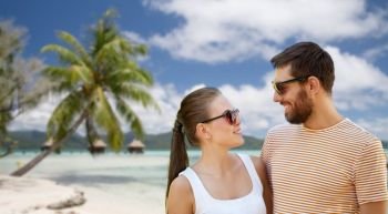 travel, tourism and people concept - happy couple in sunglasses outdoors in summer over tropical beach background in french polynesia. happy couple in sunglasses outdoors in summer