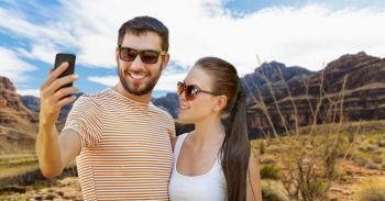 travel, tourism and technology concept - happy couple taking selfie by smartphone in summer over grand canyon national park background. couple taking selfie by smartphone on grand canyon