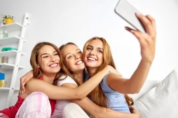 friendship, pajama party and technology concept - happy friends or teenage girls taking selfie by smartphone at home. teenage girls taking selfie by smartphone at home