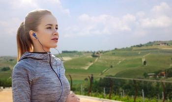fitness, sport, people, technology and lifestyle concept - happy woman running and listening to music in earphones over country landscape background. sportswoman in earphones running outdoors