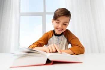 education, childhood and people concept - happy student boy reading book at home. student boy reading book at home table