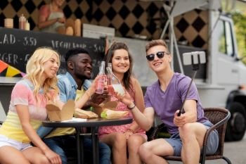 leisure, technology and people concept - happy young friends with food and drinks and taking selfie at food truck. happy young friends taking selfie at food truck