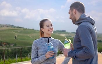 fitness, sport and people concept - smiling couple with bottles of water over country landscape background. couple with bottles of water after sports outdoors