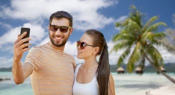 travel, tourism and people concept - happy couple taking selfie by smartphone over tropical beach background in french polynesia. happy couple taking selfie by smartphone on beach