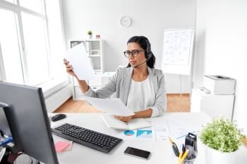 communication, business, people and technology concept - indian businesswoman or helpline operator with headset and papers at office. businesswoman with headset and papers at office
