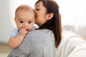 family and motherhood concept - close up of happy young asian mother kissing little baby son at home. close up of happy mother kissing baby son at home